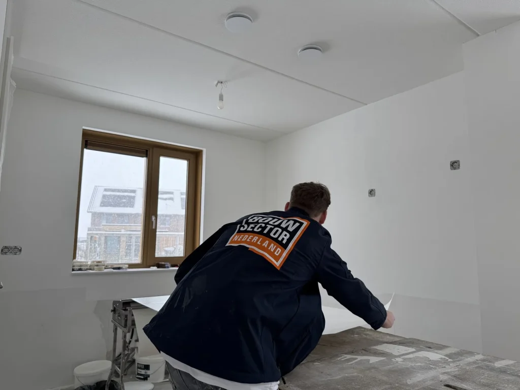Behanger van Bouwsector Nederland pakt een baan vlies van de plaktafel in een witte nieuwbouwkamer