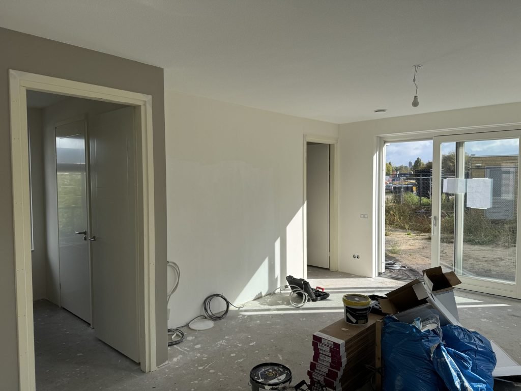 Nieuwbouwwoonkamer tijdens de afwerking, met tuindeuren en verfemmers op de dekvloer